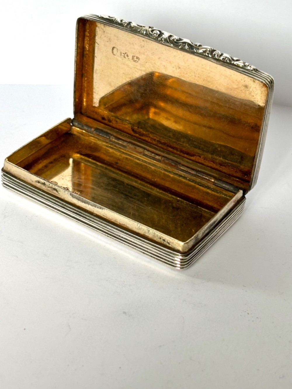 A rectangular Georgian sterling silver snuff box displaying geometric engine-turned patterns, a blank central cartouche, and reeded side edges. View II