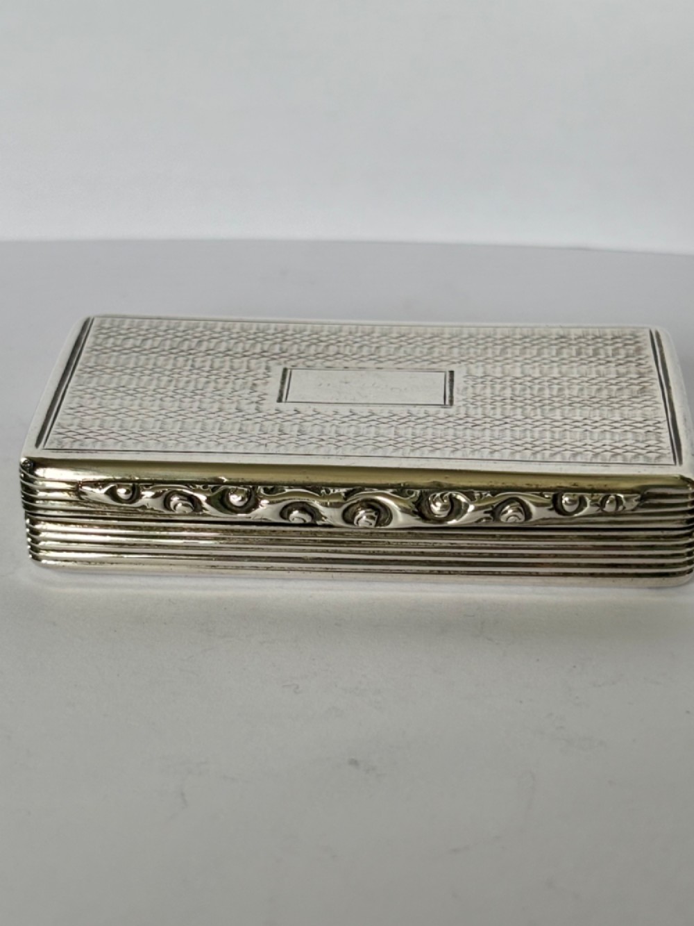 A rectangular Georgian sterling silver snuff box displaying geometric engine-turned patterns, a blank central cartouche, and reeded side edges. View III