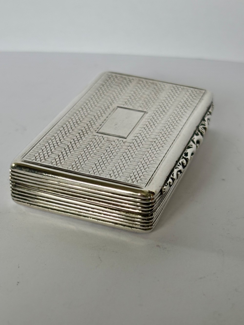 A rectangular Georgian sterling silver snuff box displaying geometric engine-turned patterns, a blank central cartouche, and reeded side edges. View IV