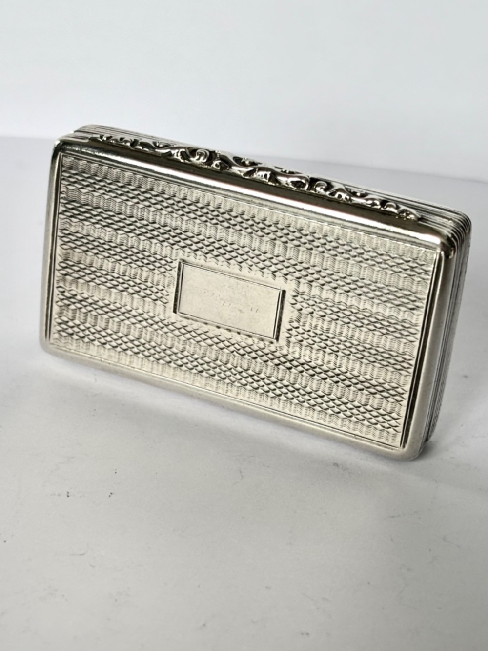 A rectangular Georgian sterling silver snuff box displaying geometric engine-turned patterns, a blank central cartouche, and reeded side edges. View V