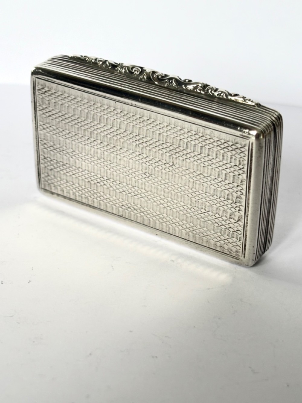 A rectangular Georgian sterling silver snuff box displaying geometric engine-turned patterns, a blank central cartouche, and reeded side edges. View VI