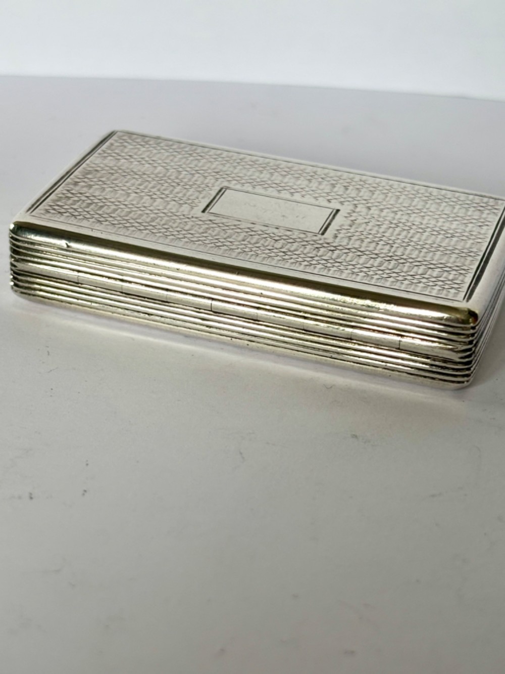 A rectangular Georgian sterling silver snuff box displaying geometric engine-turned patterns, a blank central cartouche, and reeded side edges. View X