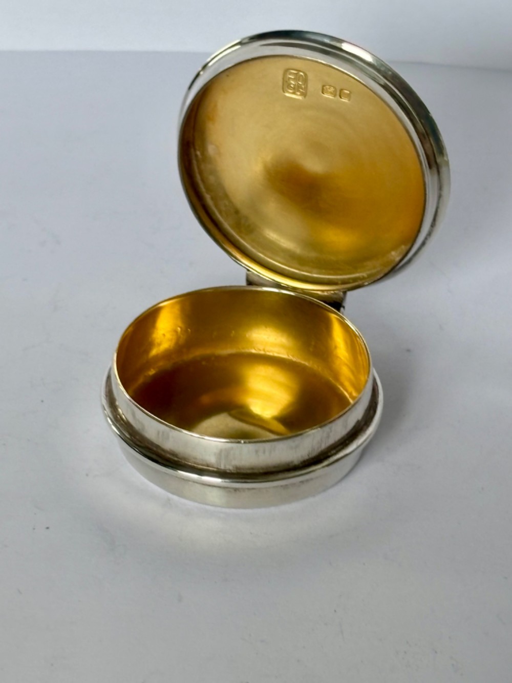 A circular sterling silver pyx box with a polished finish, featuring a lid topped with a cross and orb finial. View III