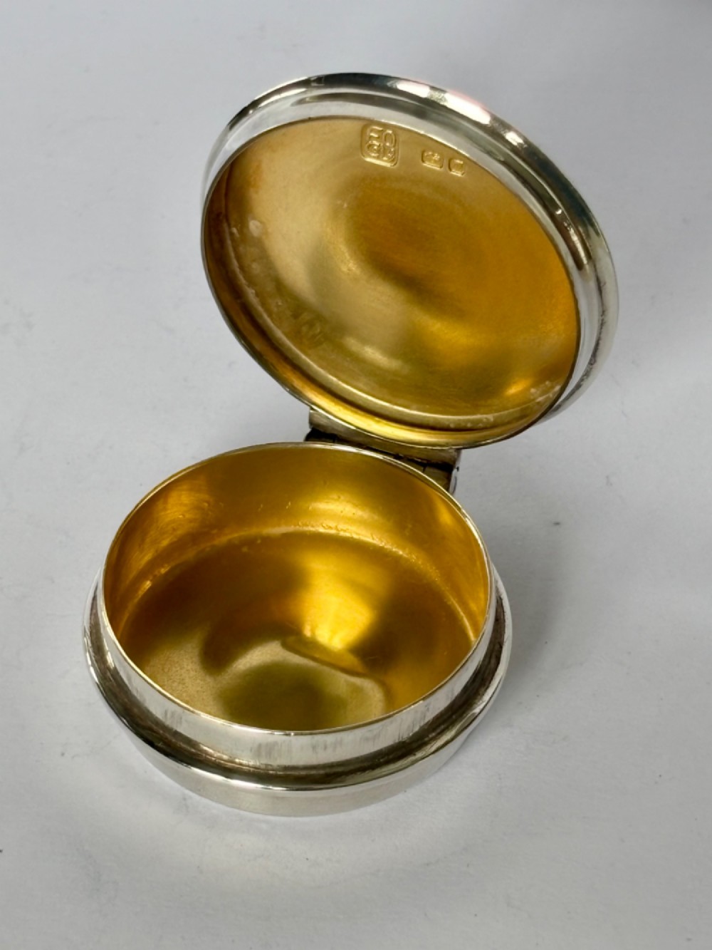 A circular sterling silver pyx box with a polished finish, featuring a lid topped with a cross and orb finial. View V