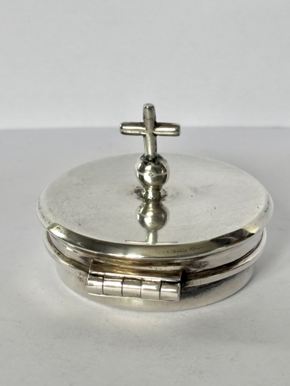 A circular sterling silver pyx box with a polished finish, featuring a lid topped with a cross and orb finial. View VIII
