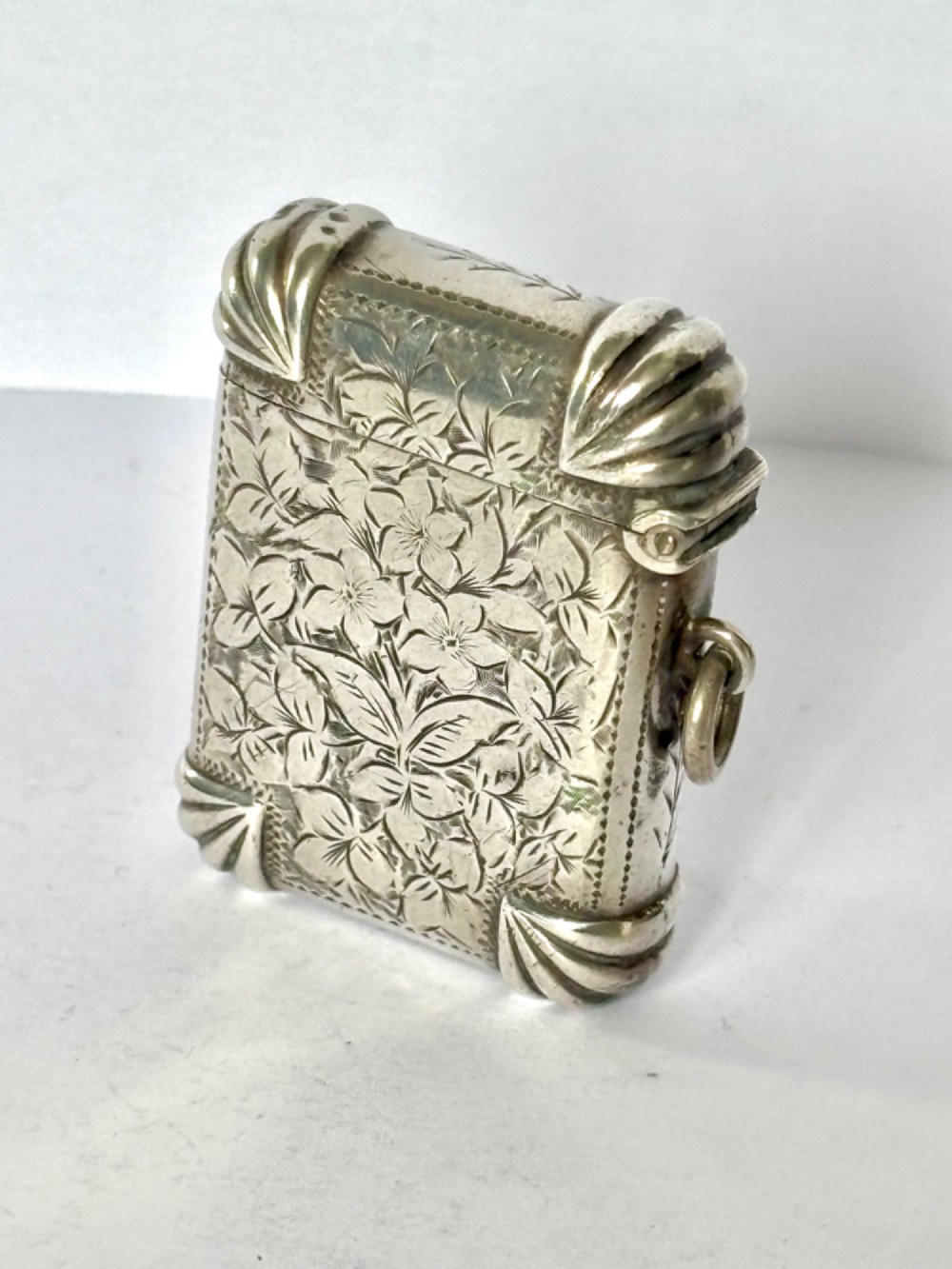 A Victorian sterling silver vesta case featuring hand-engraved floral leaf motifs, gadrooned corners, a vacant central cartouche, and a side suspension ring. View II