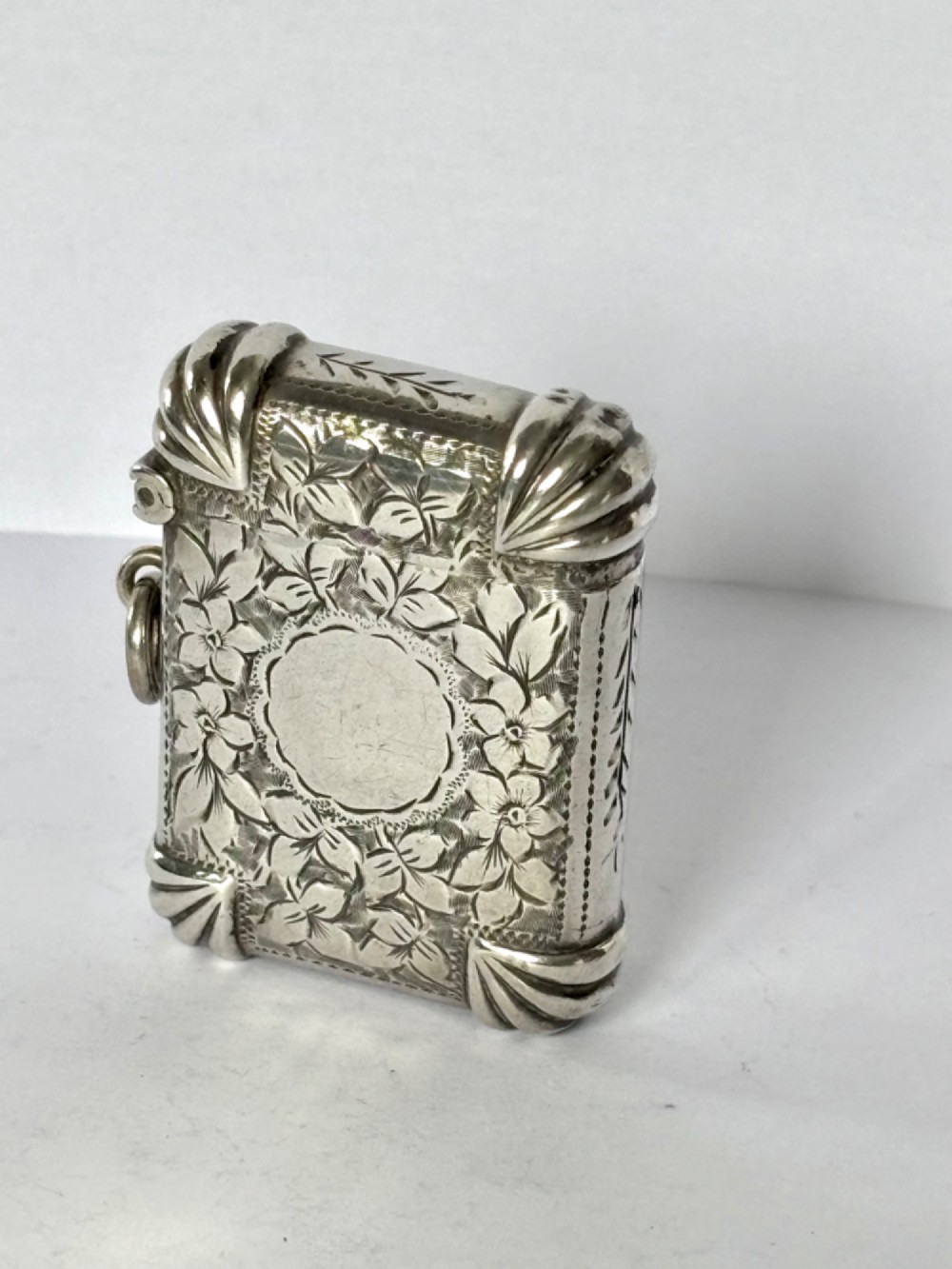 A Victorian sterling silver vesta case featuring hand-engraved floral leaf motifs, gadrooned corners, a vacant central cartouche, and a side suspension ring. View IV