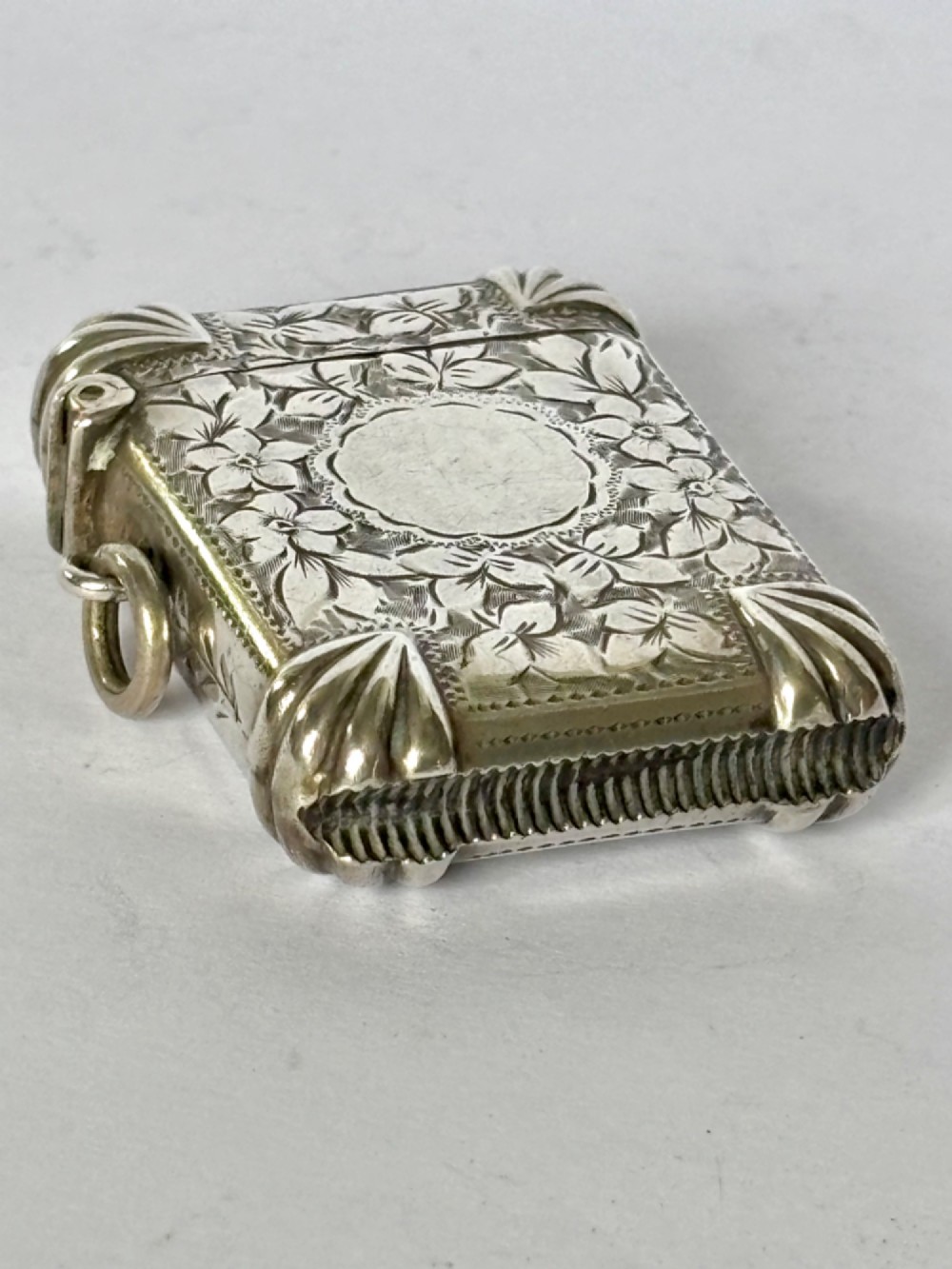 A Victorian sterling silver vesta case featuring hand-engraved floral leaf motifs, gadrooned corners, a vacant central cartouche, and a side suspension ring. View VII