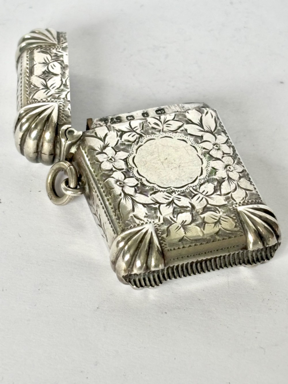 A Victorian sterling silver vesta case featuring hand-engraved floral leaf motifs, gadrooned corners, a vacant central cartouche, and a side suspension ring. View VIII