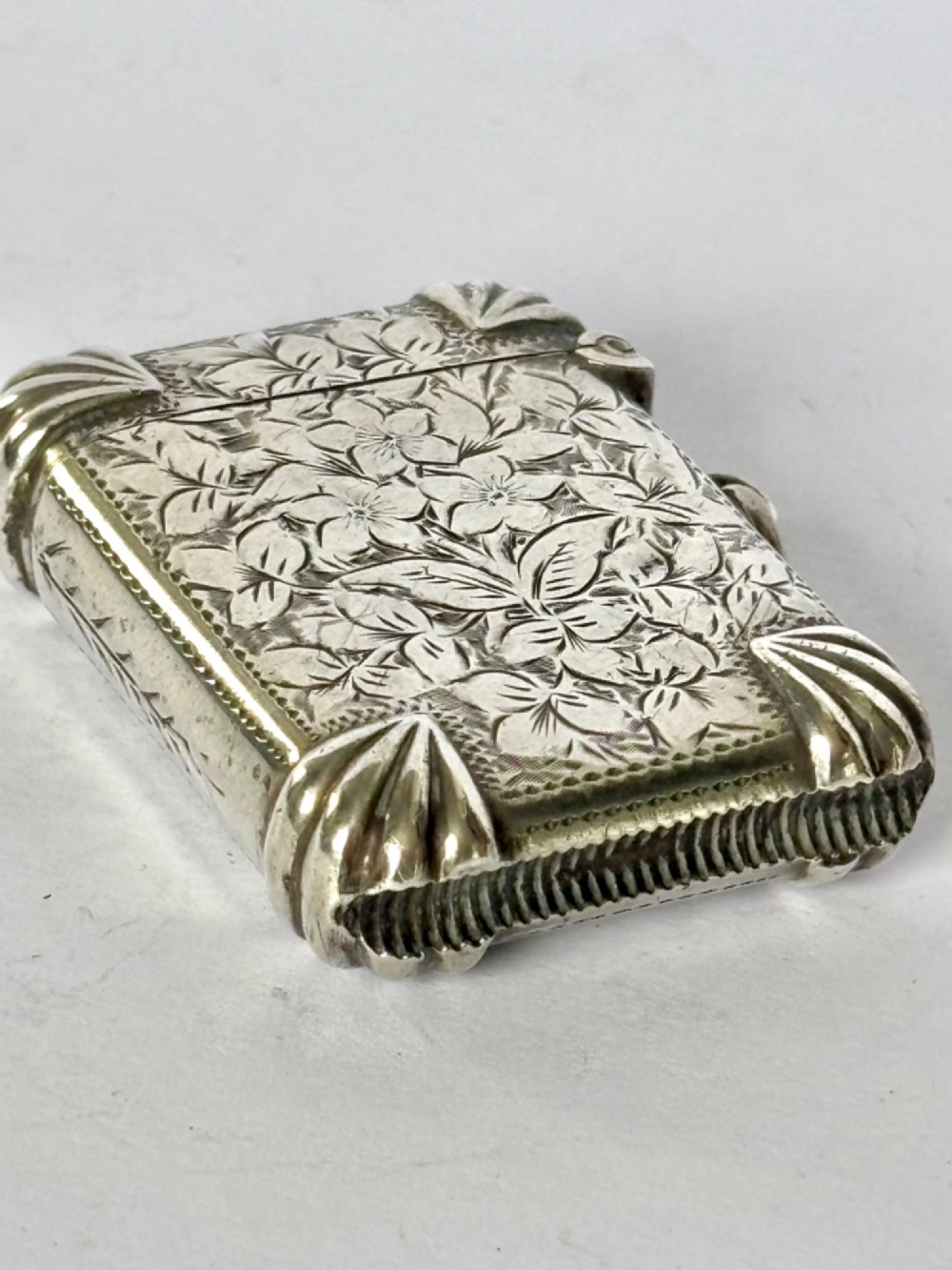 A Victorian sterling silver vesta case featuring hand-engraved floral leaf motifs, gadrooned corners, a vacant central cartouche, and a side suspension ring. View IX