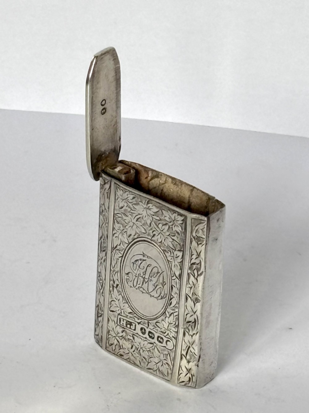 An upright rectangular Victorian sterling silver vesta case with hand-engraved leaf patterns, a central monogrammed oval cartouche, and prominent Birmingham hallmark stamps. View II