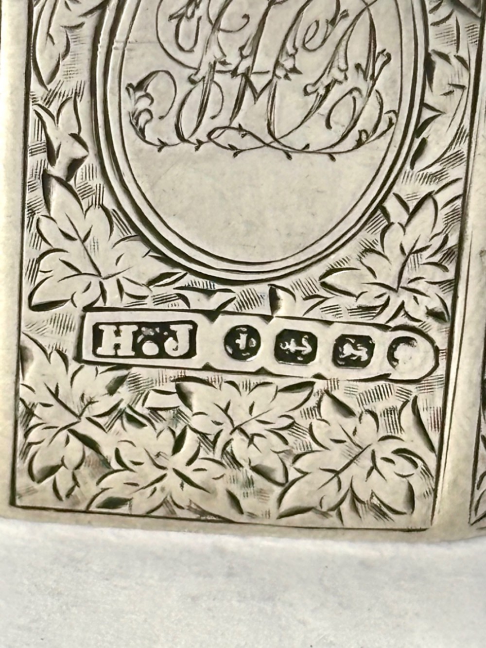 An upright rectangular Victorian sterling silver vesta case with hand-engraved leaf patterns, a central monogrammed oval cartouche, and prominent Birmingham hallmark stamps. View III