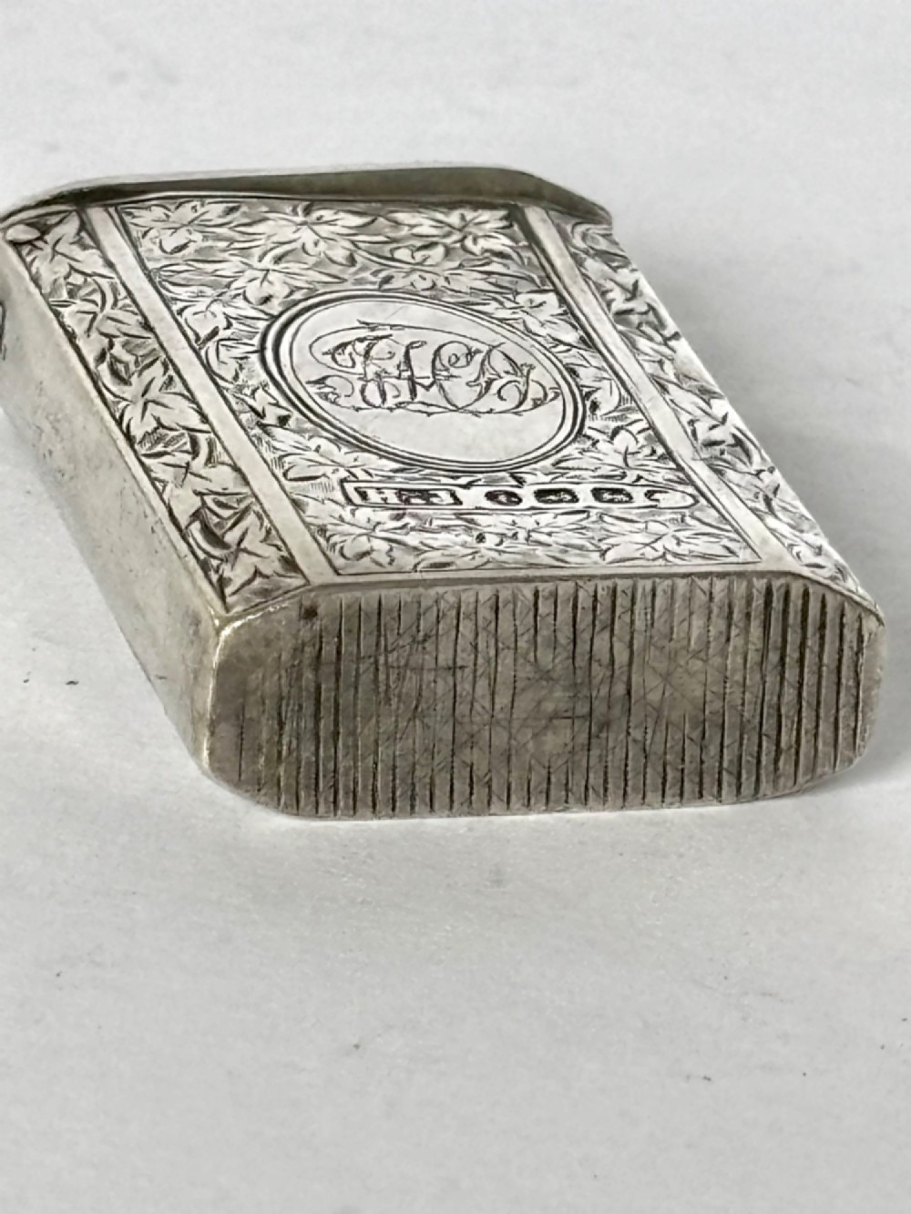 An upright rectangular Victorian sterling silver vesta case with hand-engraved leaf patterns, a central monogrammed oval cartouche, and prominent Birmingham hallmark stamps. View IV