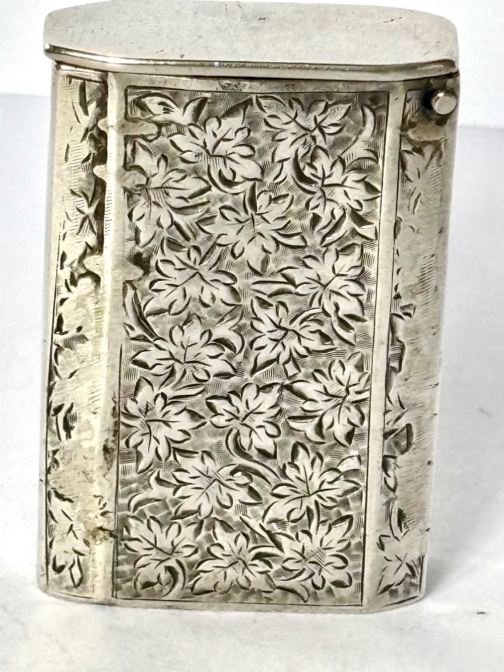 An upright rectangular Victorian sterling silver vesta case with hand-engraved leaf patterns, a central monogrammed oval cartouche, and prominent Birmingham hallmark stamps. View VI