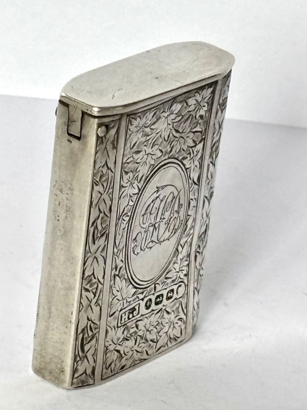 An upright rectangular Victorian sterling silver vesta case with hand-engraved leaf patterns, a central monogrammed oval cartouche, and prominent Birmingham hallmark stamps. View VII