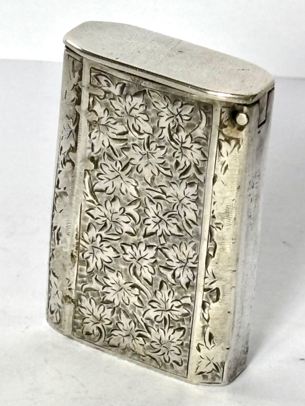 An upright rectangular Victorian sterling silver vesta case with hand-engraved leaf patterns, a central monogrammed oval cartouche, and prominent Birmingham hallmark stamps. View VIII