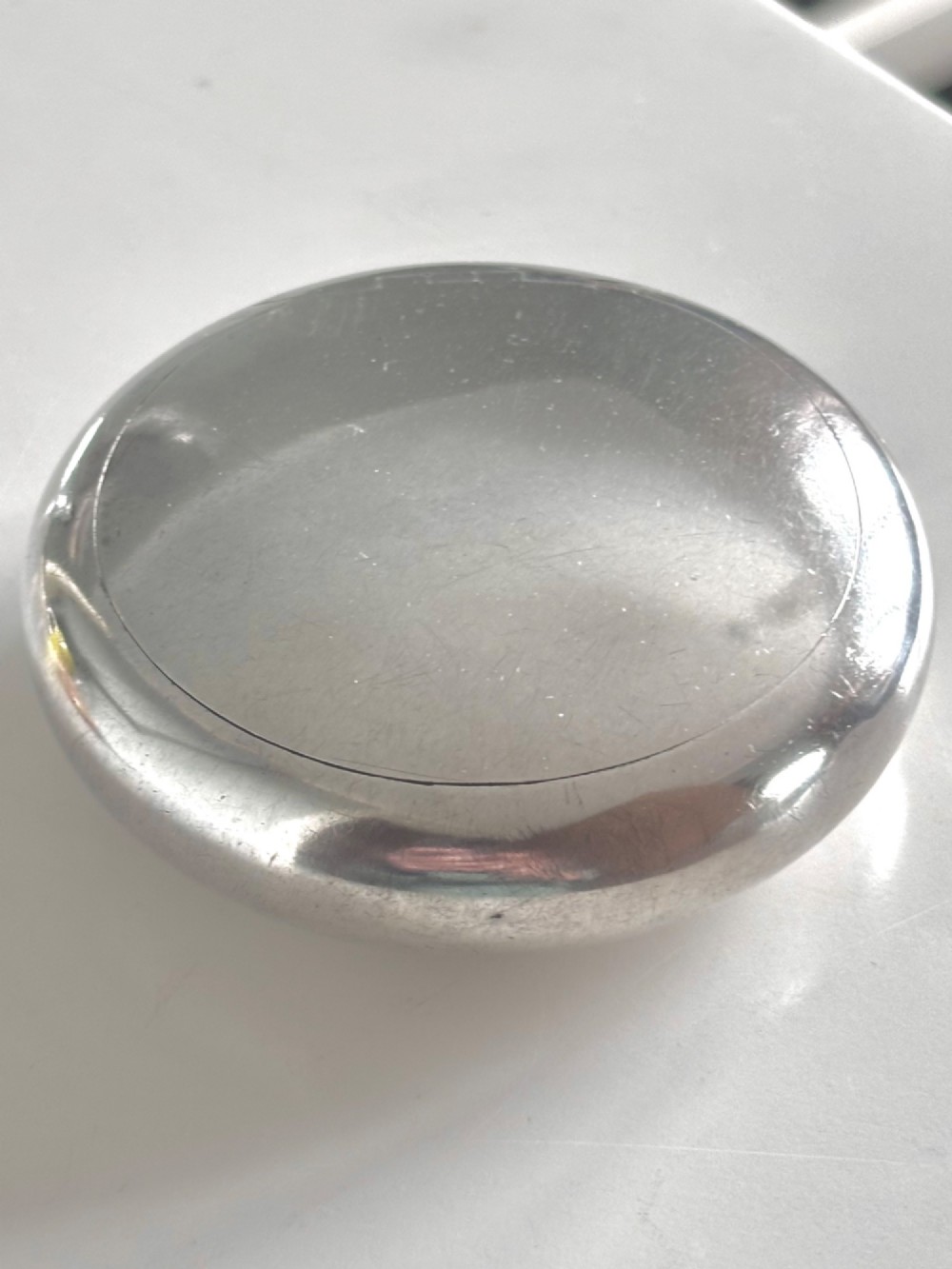 An Edwardian oval sterling silver squeeze tobacco box with a polished finish and rounded pebble profile.
