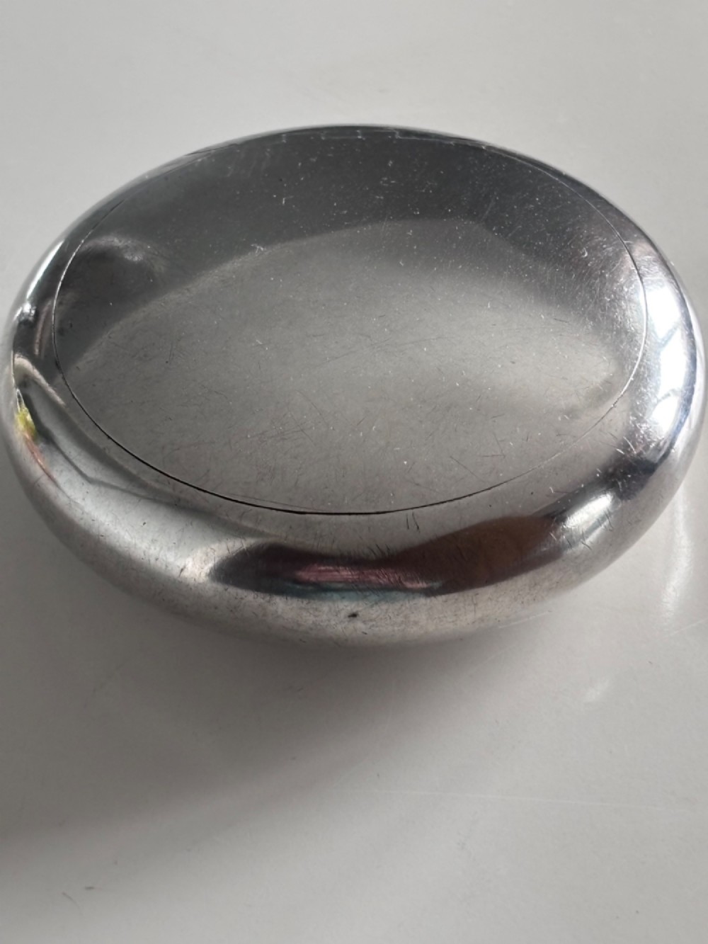 An Edwardian oval sterling silver squeeze tobacco box with a polished finish and rounded pebble profile. View V