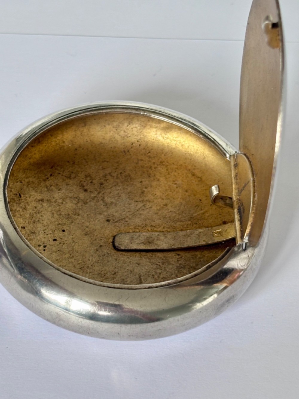An Edwardian oval sterling silver squeeze tobacco box with a polished finish and rounded pebble profile. View IX