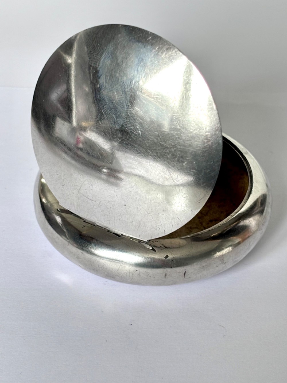 An Edwardian oval sterling silver squeeze tobacco box with a polished finish and rounded pebble profile. View X