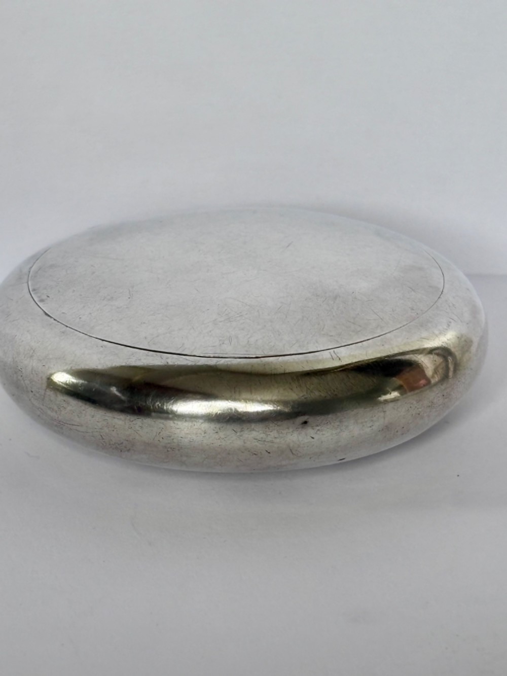 An Edwardian oval sterling silver squeeze tobacco box with a polished finish and rounded pebble profile. View XII