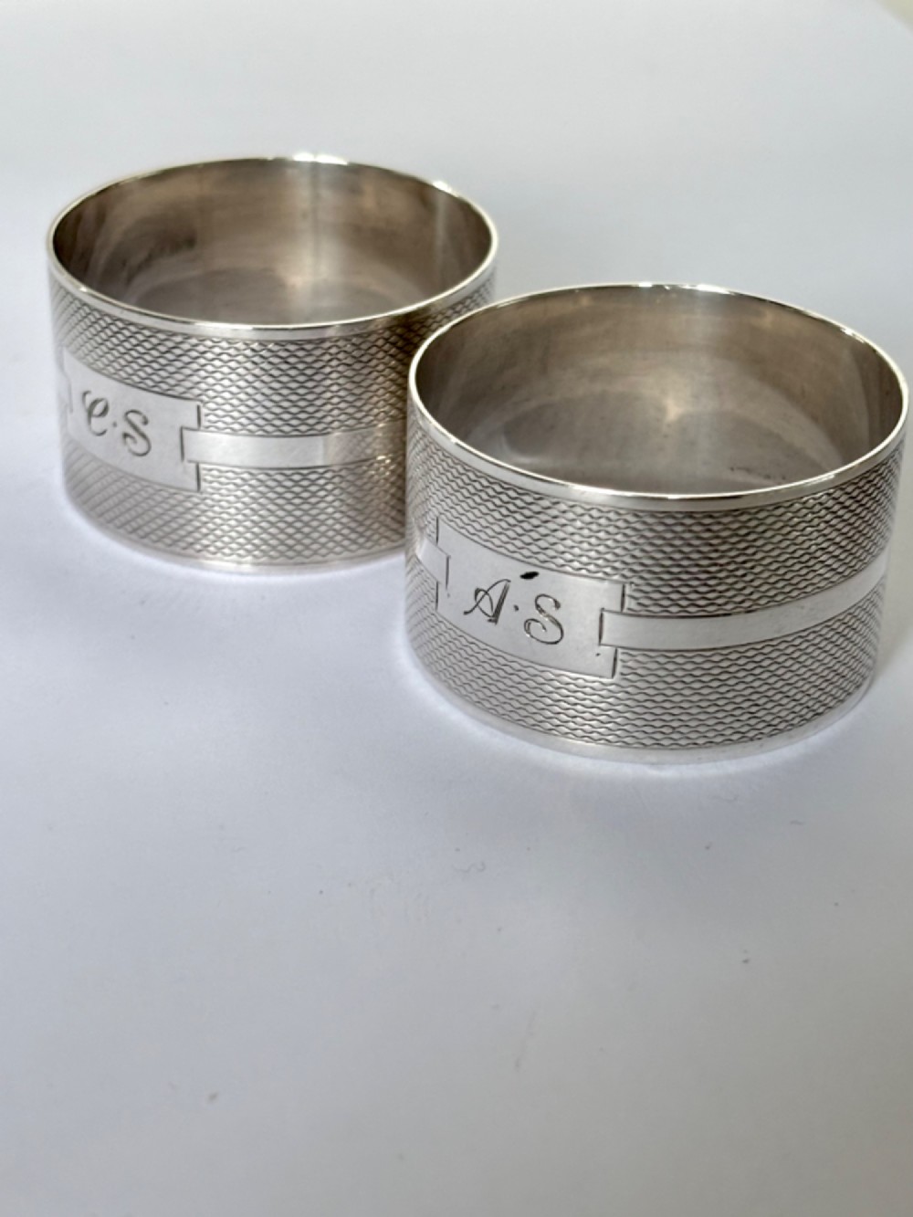 A pair of circular sterling silver napkin rings featuring an engine-turned textured pattern with a central polished band and British hallmarks. View II
