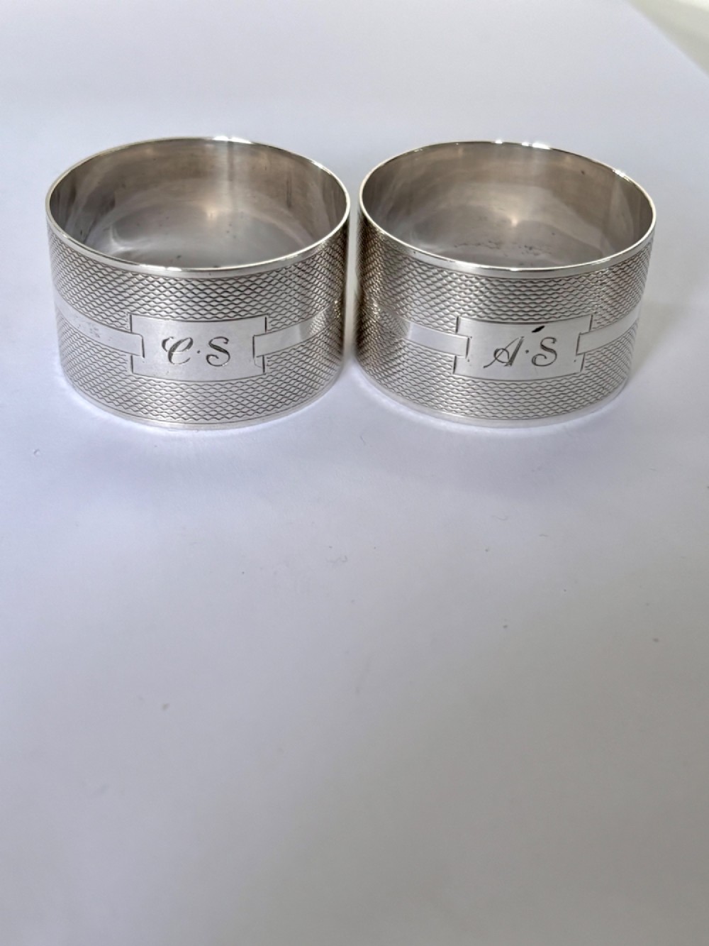 A pair of circular sterling silver napkin rings featuring an engine-turned textured pattern with a central polished band and British hallmarks. View III