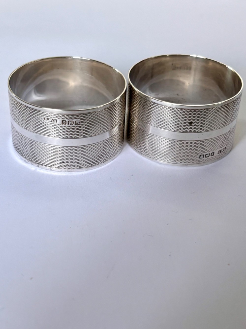A pair of circular sterling silver napkin rings featuring an engine-turned textured pattern with a central polished band and British hallmarks. View IV
