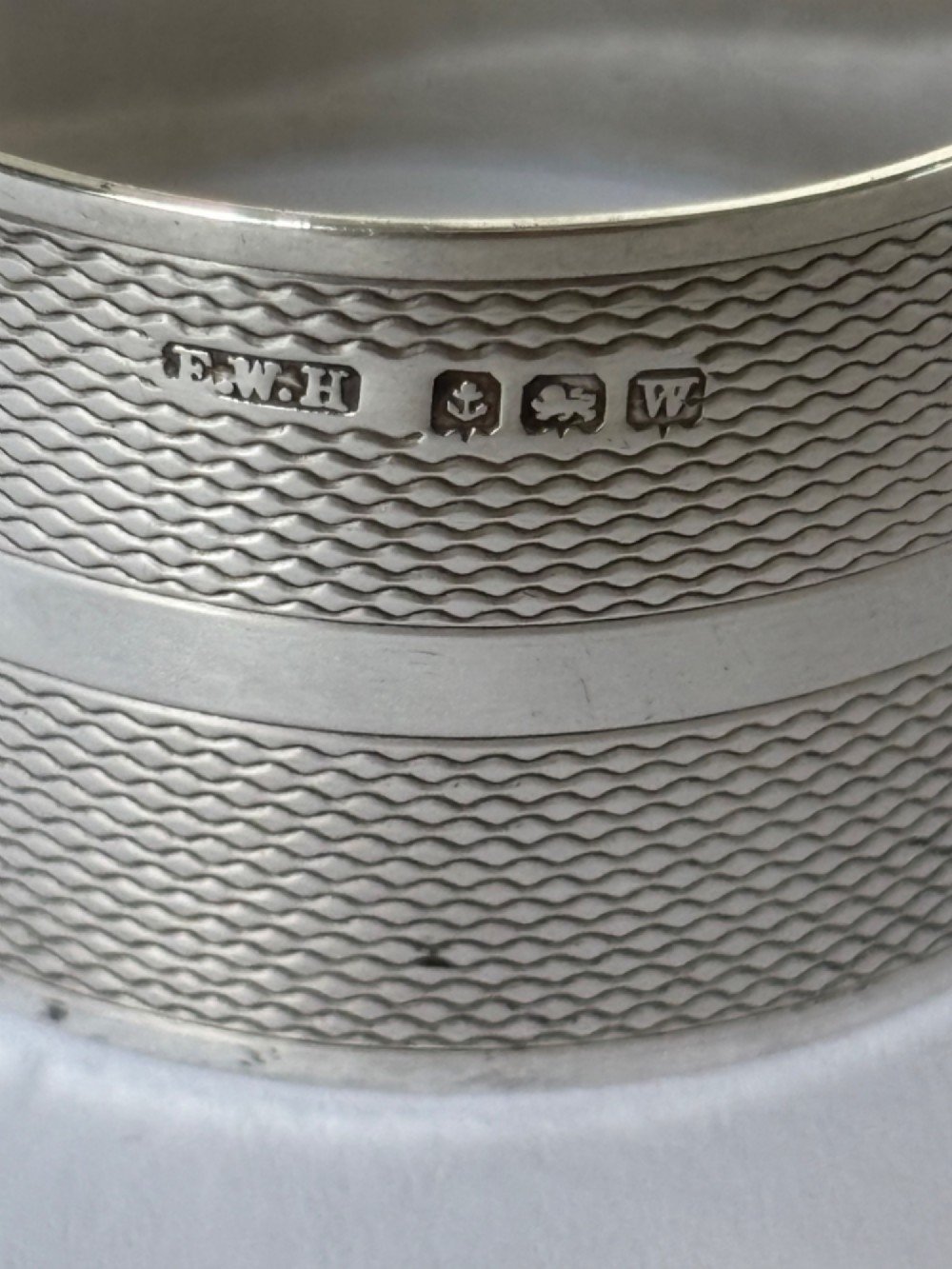 A pair of circular sterling silver napkin rings featuring an engine-turned textured pattern with a central polished band and British hallmarks. View V