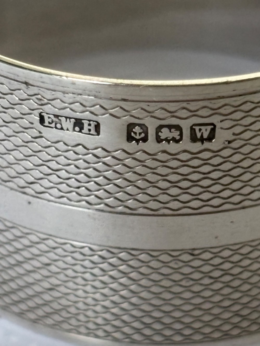 A pair of circular sterling silver napkin rings featuring an engine-turned textured pattern with a central polished band and British hallmarks. View VI