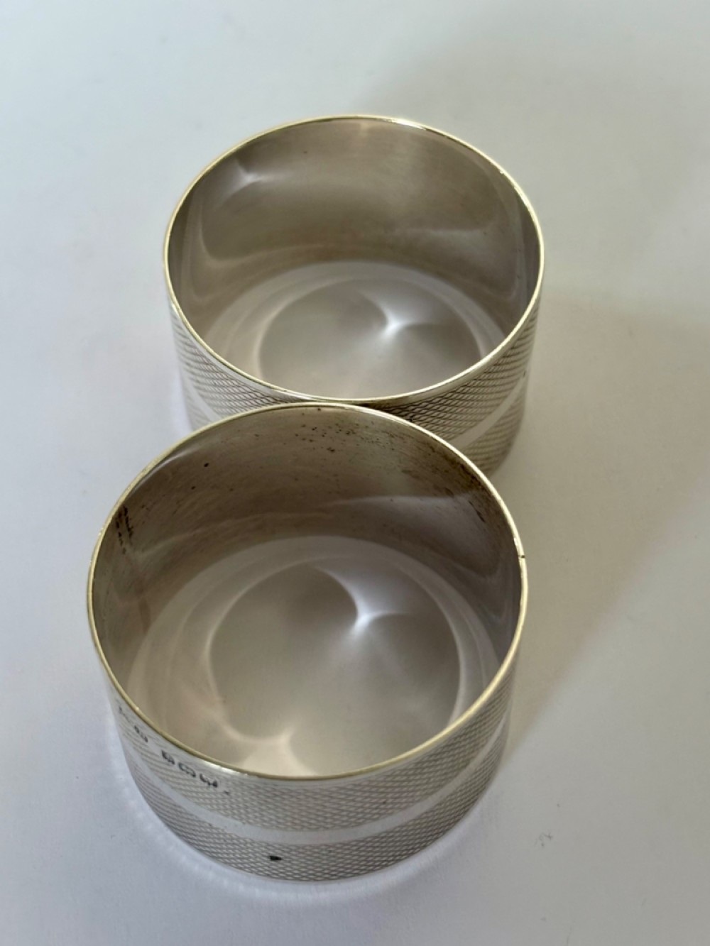 A pair of circular sterling silver napkin rings featuring an engine-turned textured pattern with a central polished band and British hallmarks. View VII