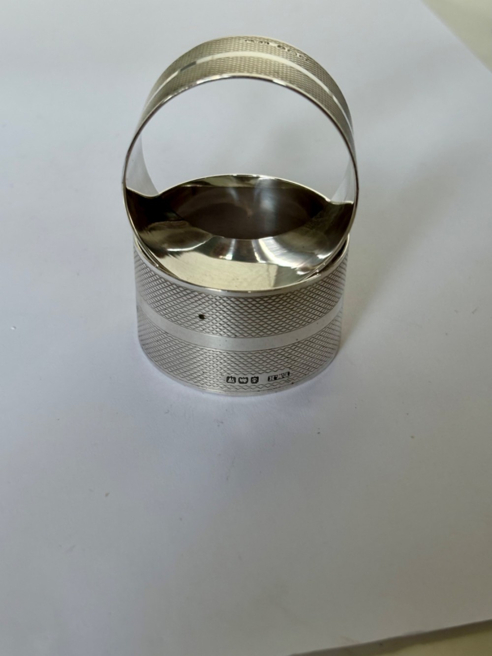 A pair of circular sterling silver napkin rings featuring an engine-turned textured pattern with a central polished band and British hallmarks. View VIII