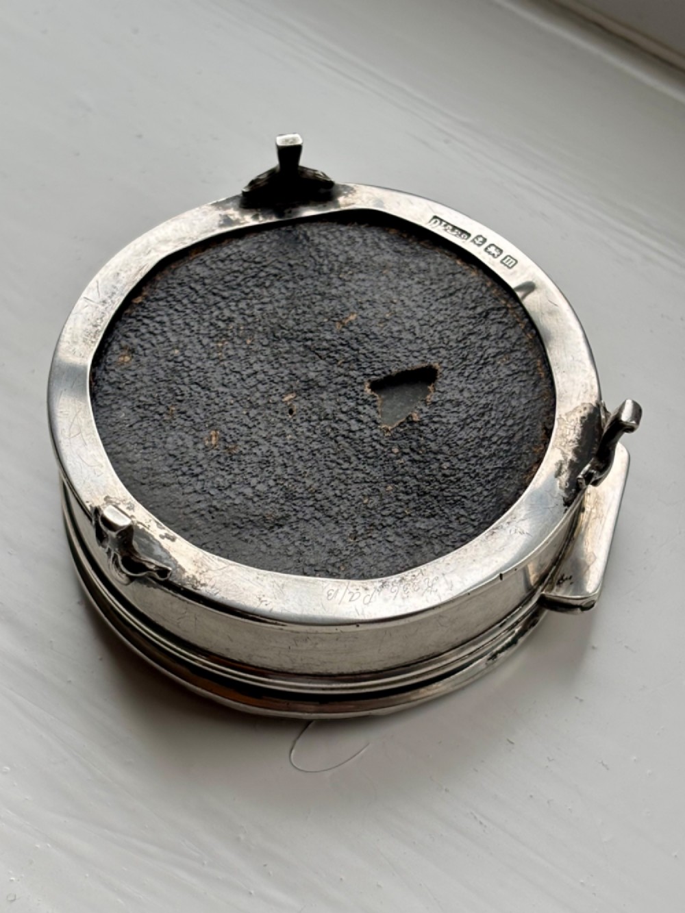 A circular silver dressing table box featuring a dark tortoiseshell lid with silver floral basket inlay resting on small shaped feet. View VI