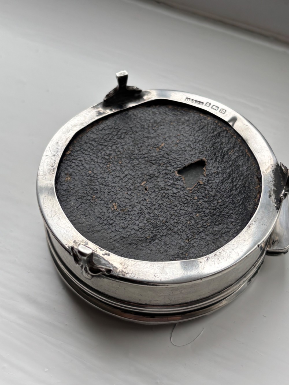 A circular silver dressing table box featuring a dark tortoiseshell lid with silver floral basket inlay resting on small shaped feet. View XIII