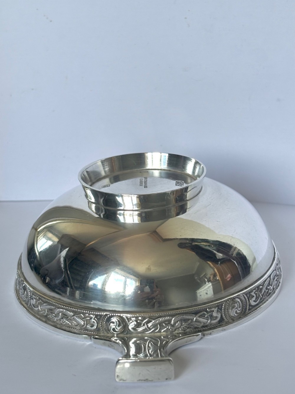 A shallow sterling silver quaich featuring two flattened lug handles, a circular pedestal base, and a band of embossed Celtic knotwork along the upper rim. View V