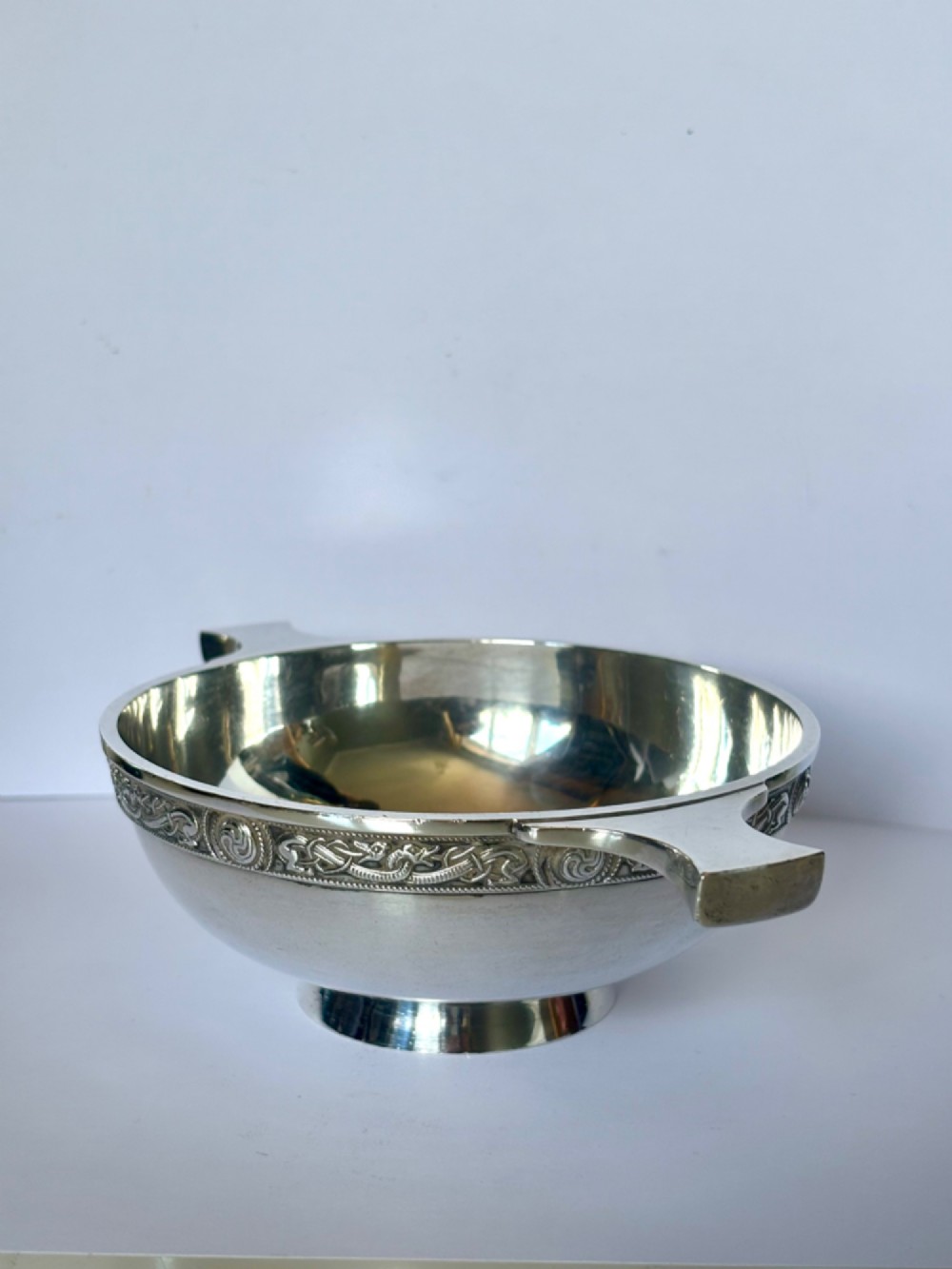 A shallow sterling silver quaich featuring two flattened lug handles, a circular pedestal base, and a band of embossed Celtic knotwork along the upper rim. View VIII