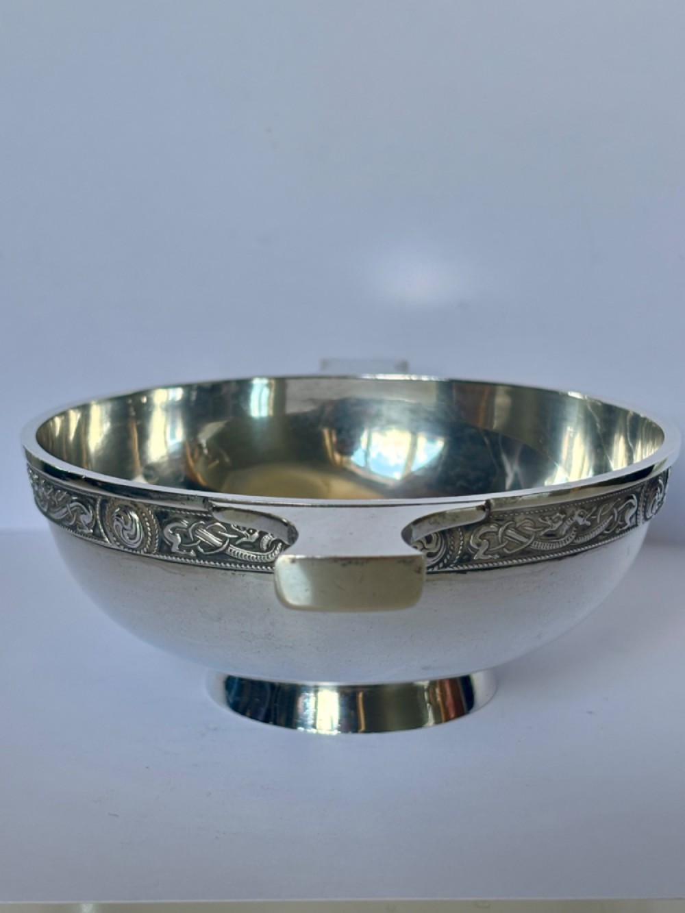 A shallow sterling silver quaich featuring two flattened lug handles, a circular pedestal base, and a band of embossed Celtic knotwork along the upper rim. View XII