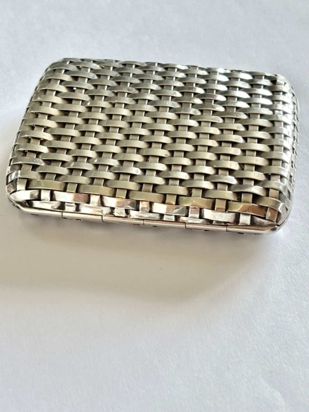 An early 20th-century rectangular silver cigarette case with a textured basketweave pattern and a side release button. View II