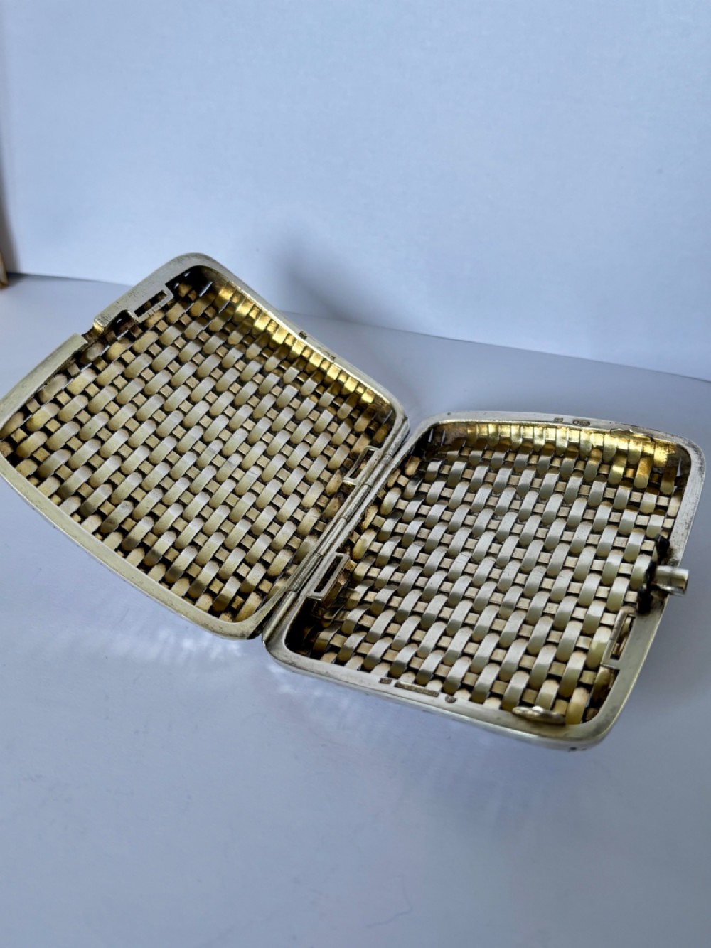 An early 20th-century rectangular silver cigarette case with a textured basketweave pattern and a side release button. View X