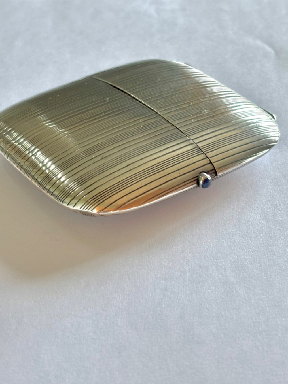 An Art Deco Continental 900 silver gilt cigarette case featuring horizontal engine-turned reeding and a blue cabochon push button.
