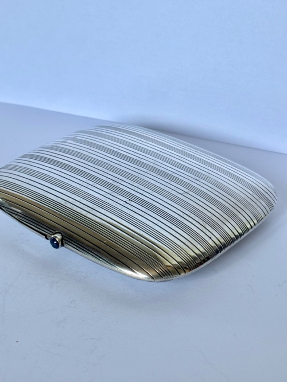 An Art Deco Continental 900 silver gilt cigarette case featuring horizontal engine-turned reeding and a blue cabochon push button. View III