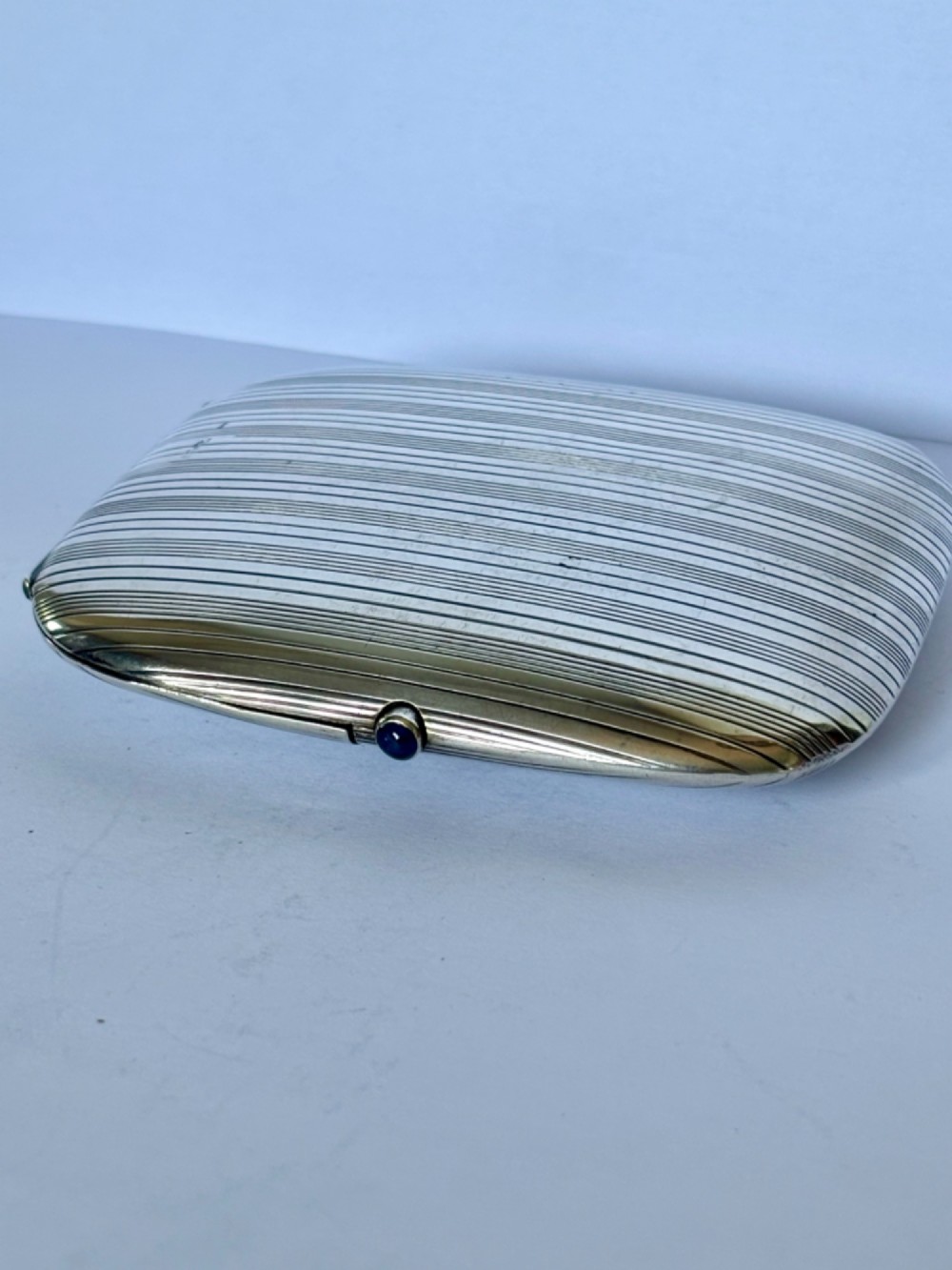 An Art Deco Continental 900 silver gilt cigarette case featuring horizontal engine-turned reeding and a blue cabochon push button. View VII