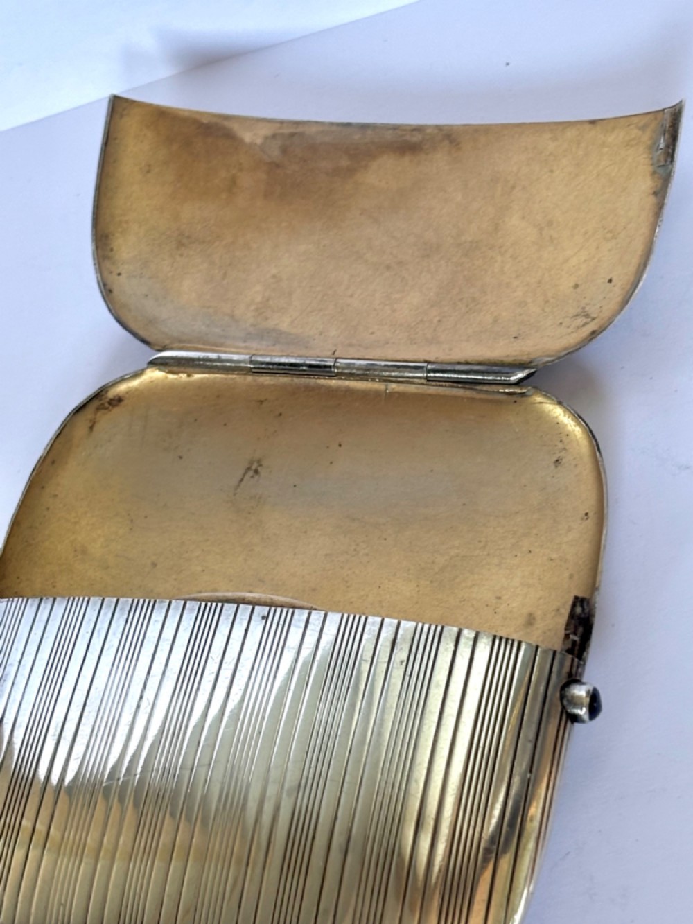 An Art Deco Continental 900 silver gilt cigarette case featuring horizontal engine-turned reeding and a blue cabochon push button. View VIII