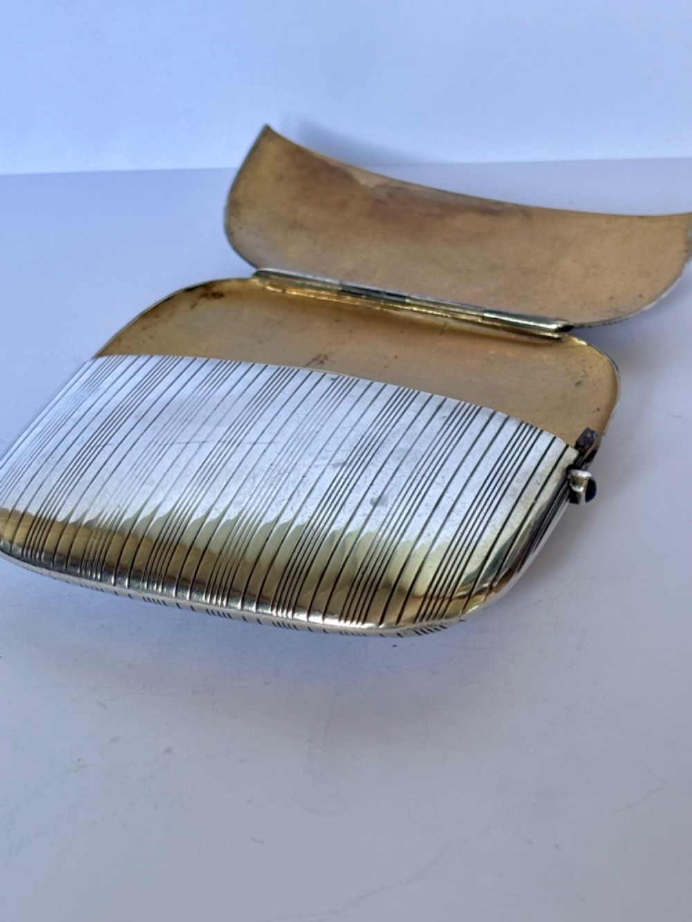 An Art Deco Continental 900 silver gilt cigarette case featuring horizontal engine-turned reeding and a blue cabochon push button. View IX