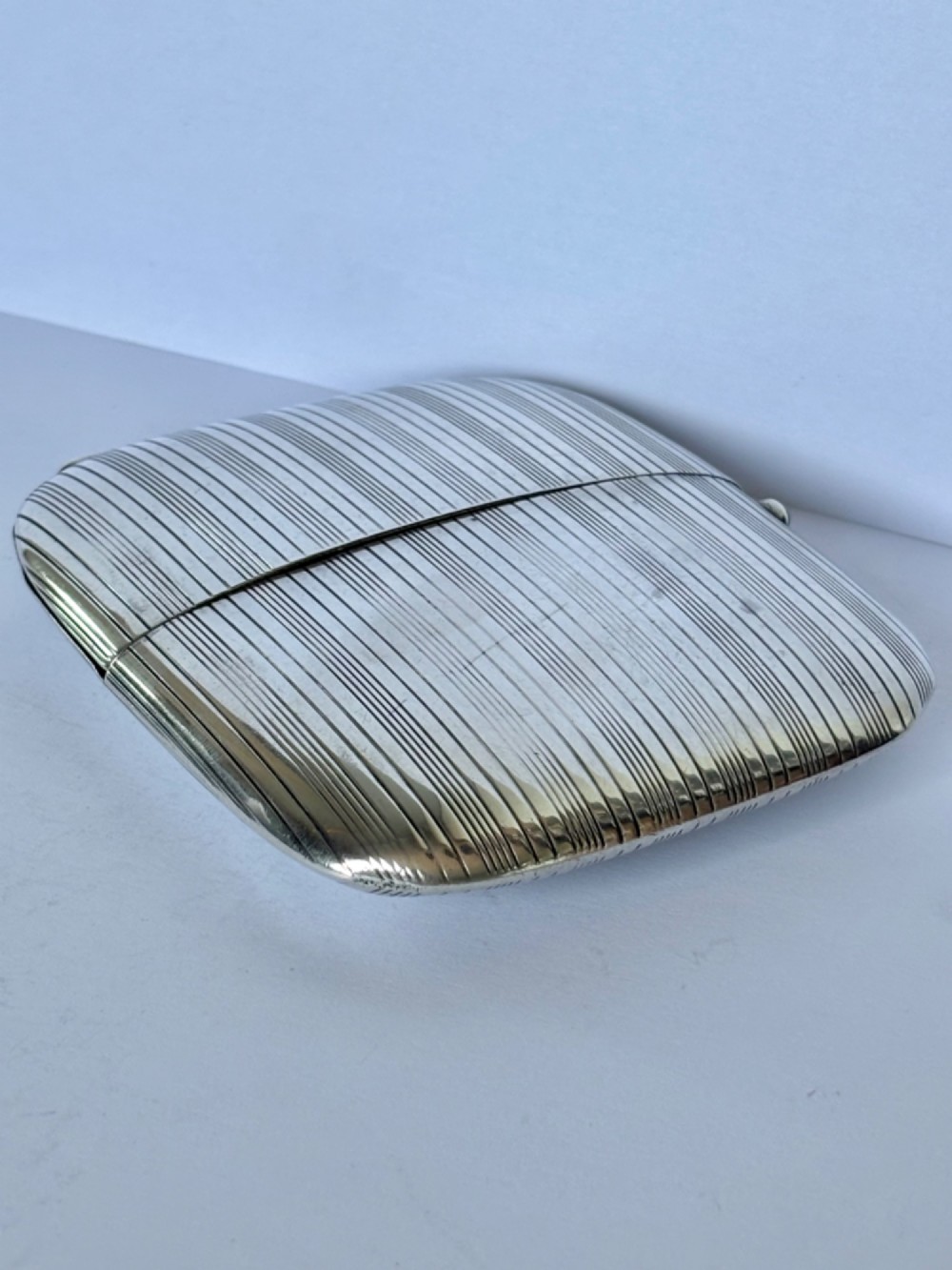 An Art Deco Continental 900 silver gilt cigarette case featuring horizontal engine-turned reeding and a blue cabochon push button. View X