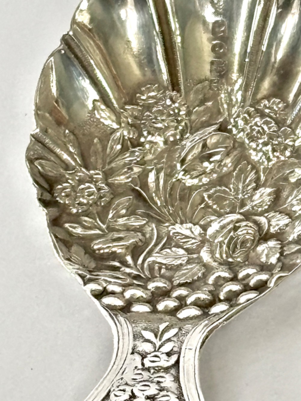A Victorian sterling silver tea caddy spoon featuring a fluted shell-shaped bowl with embossed floral detailing and a hallmarked handle. View IV