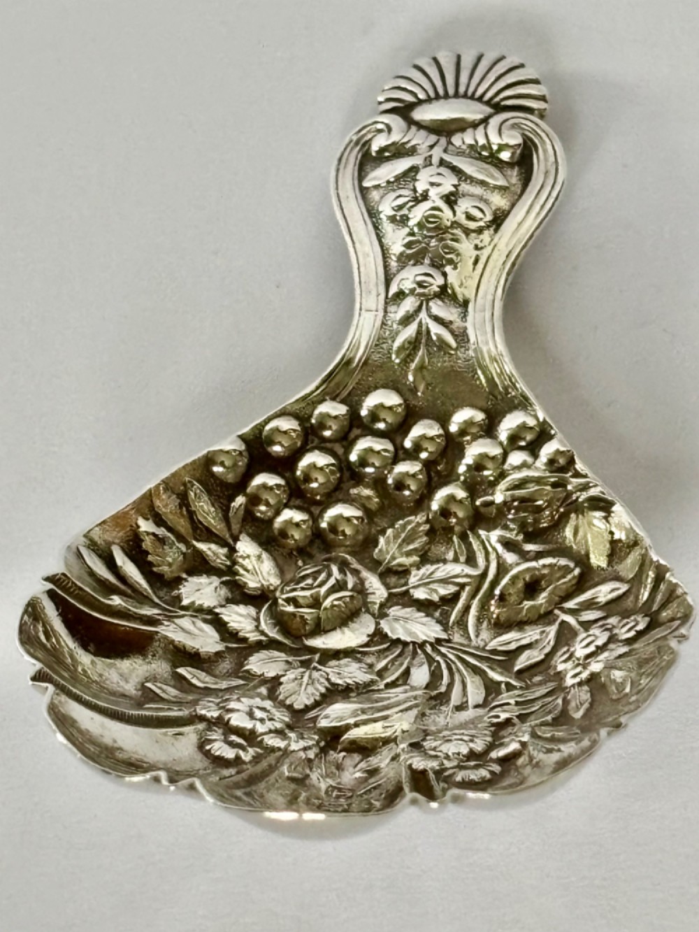 A Victorian sterling silver tea caddy spoon featuring a fluted shell-shaped bowl with embossed floral detailing and a hallmarked handle. View V