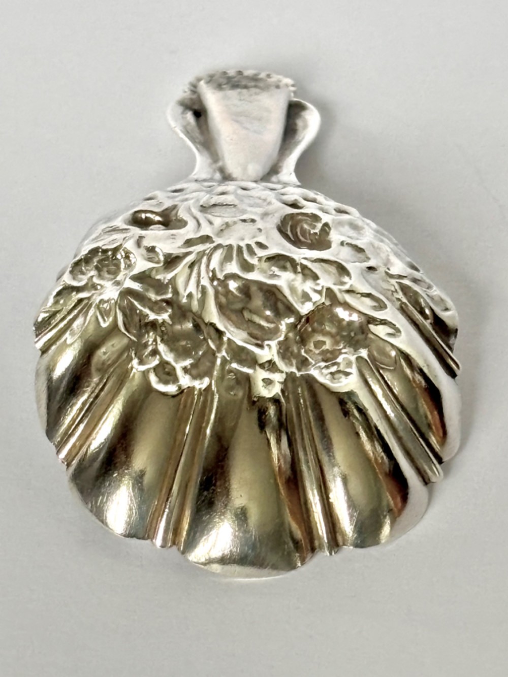 A Victorian sterling silver tea caddy spoon featuring a fluted shell-shaped bowl with embossed floral detailing and a hallmarked handle. View VI