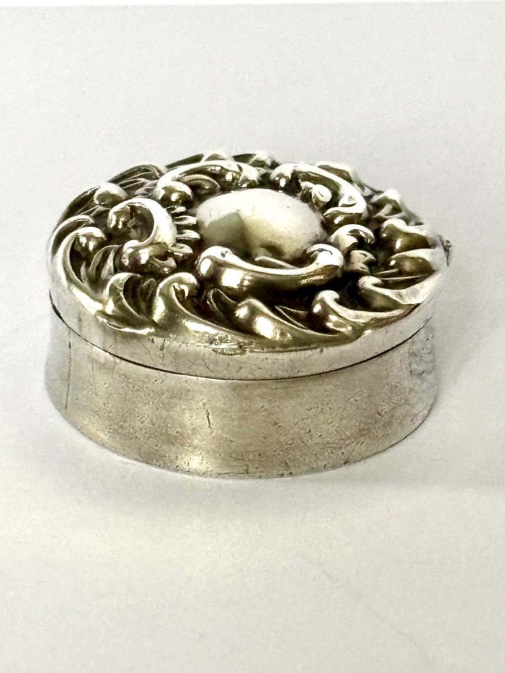 A small circular Edwardian sterling silver gilt trinket box with embossed scrollwork decoration on the lid.