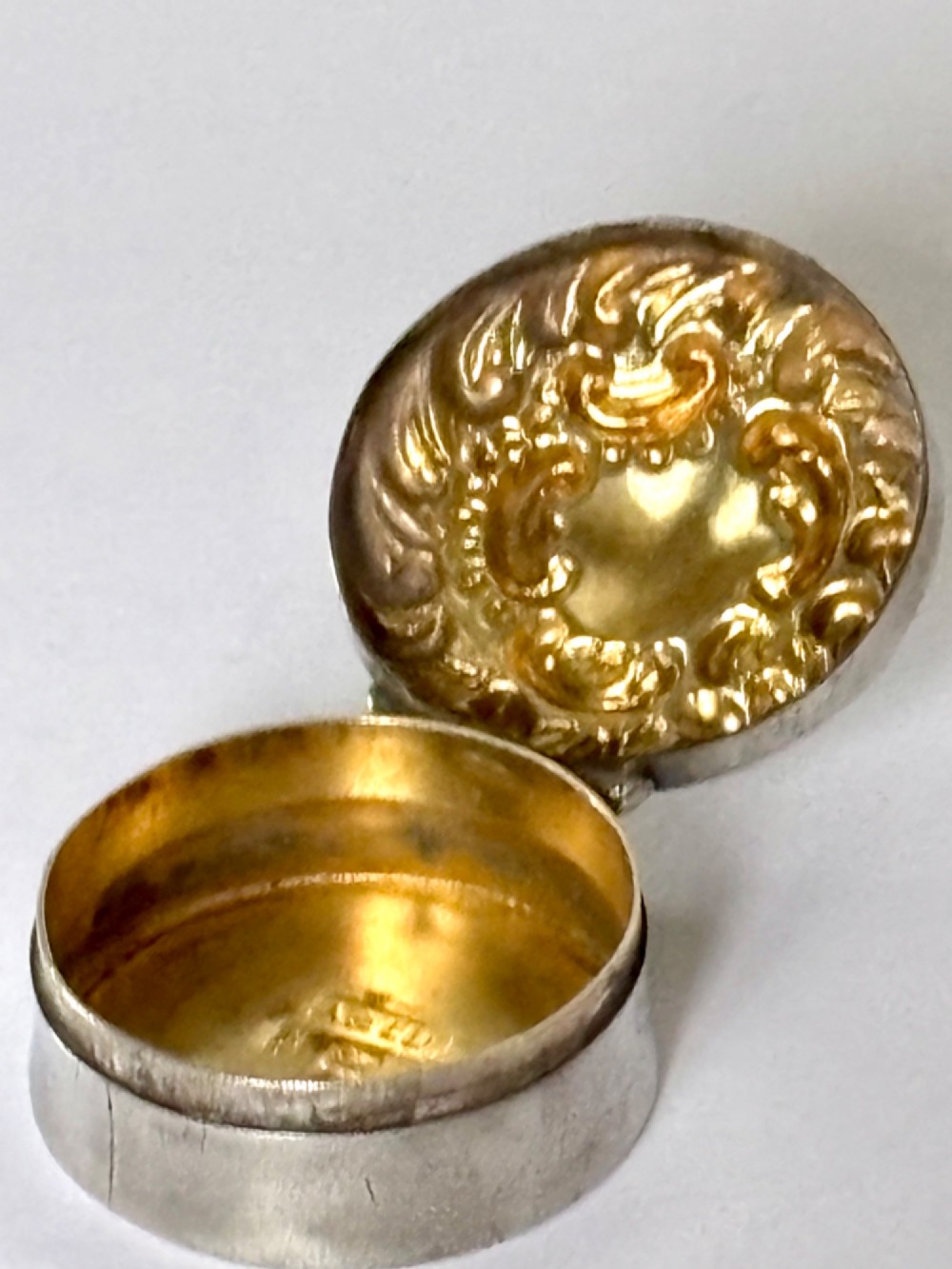 A small circular Edwardian sterling silver gilt trinket box with embossed scrollwork decoration on the lid. View II